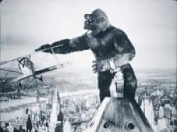Black & white phot of old seen with King Kong on top of the Empire State Building reaching for biplane