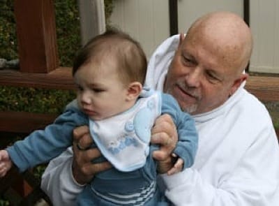 Photo of bald man, David, holding and looking at his grandchild.