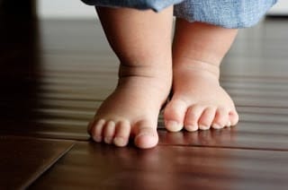 Up-close photo of baby feet standing on wood floor.