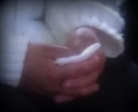 Close-up photo of a womans hands, clasped, holding a tissue.