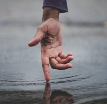 Photo of hand with finger touch surface of stream water