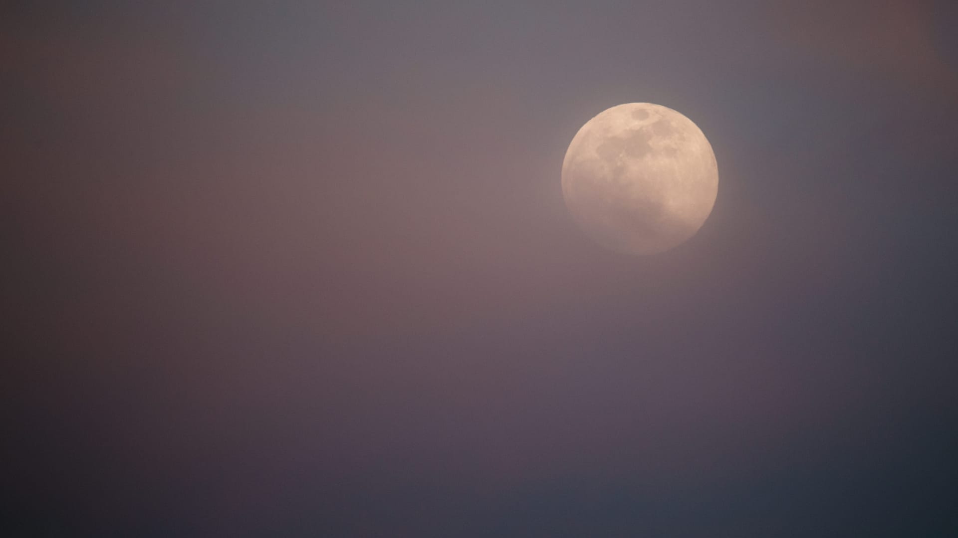 Photo of full moon in misty purple-pink night sky.