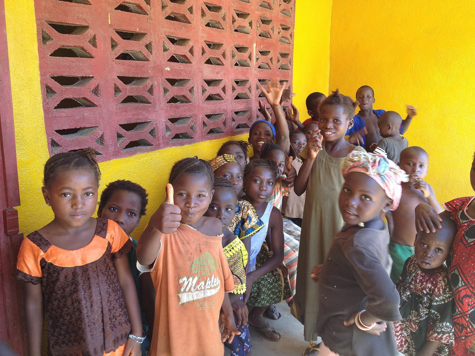 Photo of group of children, many giving a thumbs up and smiling, some serious and curious