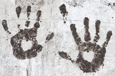 Photo of brown hand prints on white wall, with white hearts in the palms