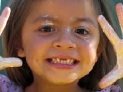 LIttle girl with smile, hands & face with bits of finger paint