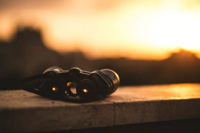 Photo of binoculars on a ledge aimed at a blurred distant sunset.